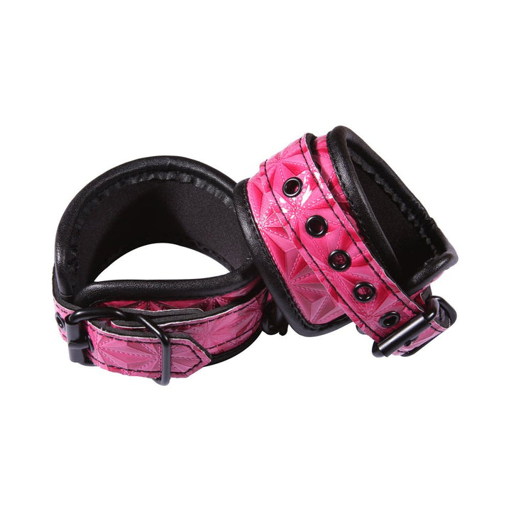 Pair of pink embossed wrist cuffs with black soft lining and black metal hardware on white background