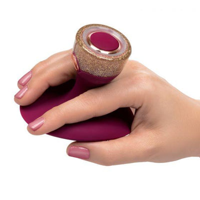 Hand holding a maroon and gold glitter handheld massager with a circular control button on top.