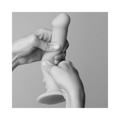 Hands demonstrating the flexibility of a silicone strap-on dildo with a suction cup base against a plain background.