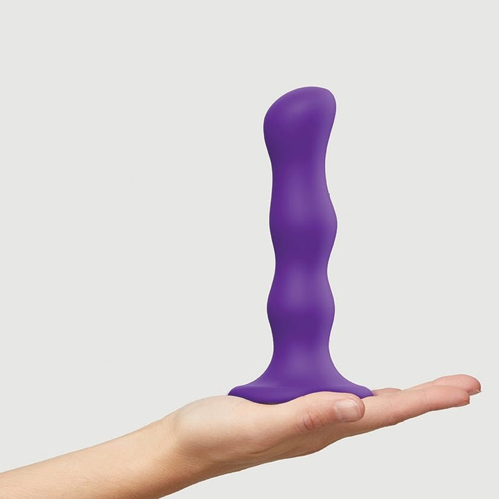 Hand holding a purple silicone dildo with ergonomic curves and a suction cup base against a plain background.