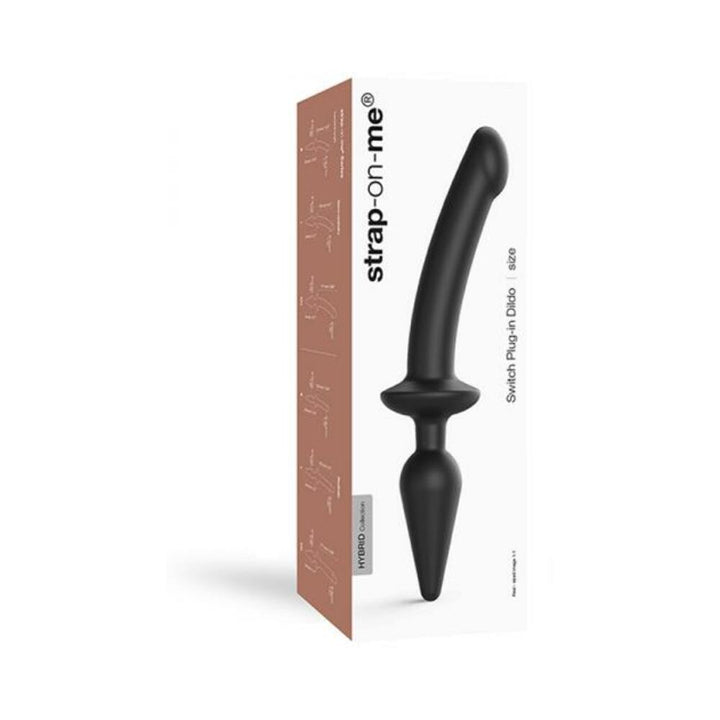 Black dual-ended strap-on dildo with plug, displayed next to its white and brown packaging box.
