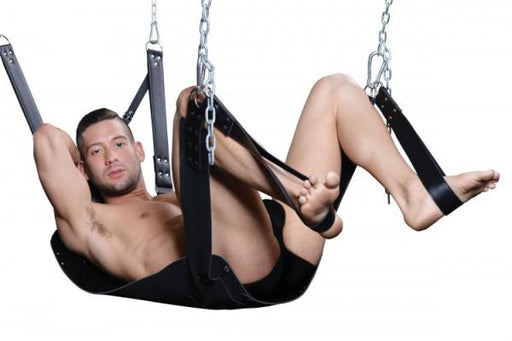 Man reclining in a black leather bondage sling with stirrups and padded headrest suspended by metal chains.
