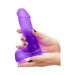 Hands holding a purple realistic dildo with suction cup base against a white background.