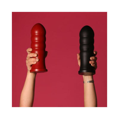 Hands holding two large textured silicone toys in red and black against a red background.