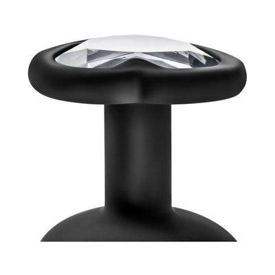 Close-up of a small black anal plug with a clear gem at the base, featuring a smooth tapered tip and neck design.