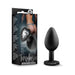 Small black silicone anal plug with a heart-shaped base featuring a clear gem, shown next to its packaging.