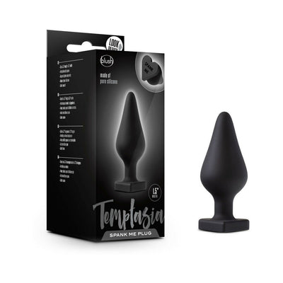 Black silicone Temptasia Spank Me butt plug with tapered shape and heart-shaped base next to its packaging box.