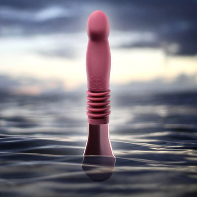 Temptasia Trixie thrusting dildo in wine color standing upright in calm water with a soft cloudy sky background.
