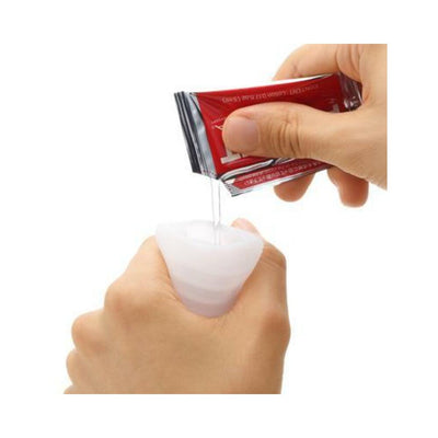 Hands applying lubricant from a small packet onto a white Tenga Pocket Masturbator Sleeve Hexa Brick.