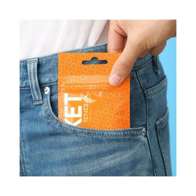 Hand placing compact orange Tenga Pocket Masturbator Sleeve Hexa Brick package into blue denim jeans pocket.