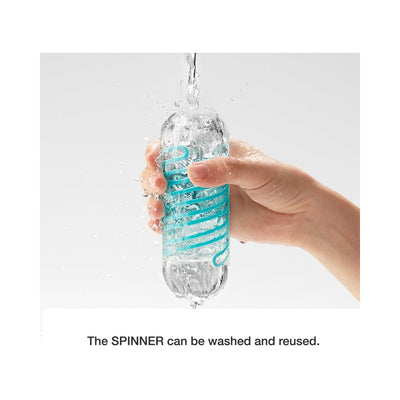 Hand holding a transparent Tenga Spinner Pixel with blue internal coil under running water, demonstrating it is washable and reusable.