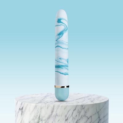 Blue and white marbled vibrator with gold accent standing on a round marble pedestal against a light blue background.