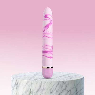 Pink and white marbled vibrator standing upright on a round marble pedestal with a soft pink gradient background.