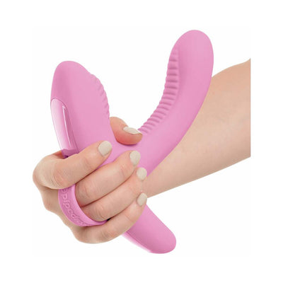 Hand holding a pink dual-motor silicone vibrator with textured flexible arms designed for targeted stimulation.