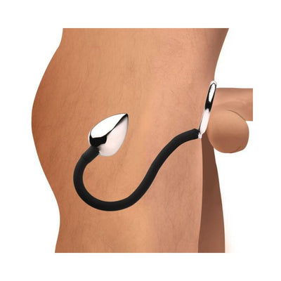 Side view of a male torso wearing a metal anal plug connected by a black silicone cord to a metal cock and ball ring.