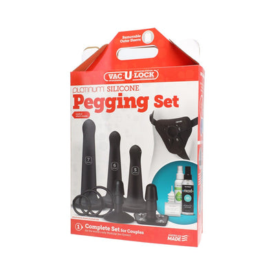 Vac-U-Lock Silicone Pegging Set packaging showing three black silicone attachments, harness, rings, lubricant, cleaner, and powders.
