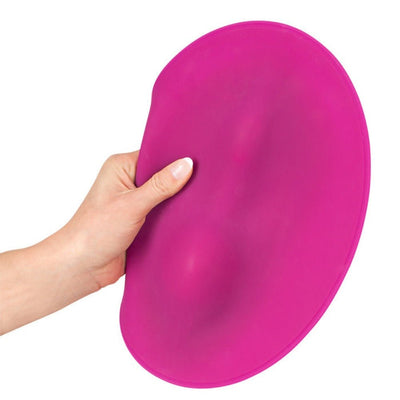 Hand holding a flexible, oval-shaped magenta silicone VibePad with subtle raised contours.