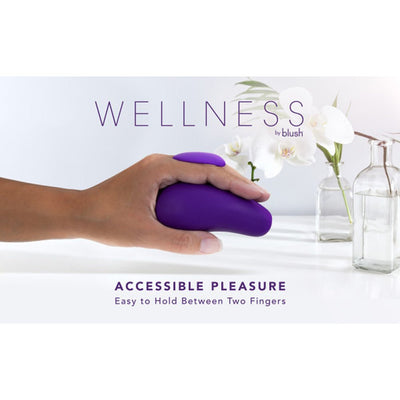 Hand holding a purple Wellness Palm Sense massager with finger fin, displayed with white orchids and glass vases in background.