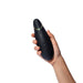 Hand holding a sleek black Womanizer Premium 2 clitoral stimulator with gold accent and control buttons visible.