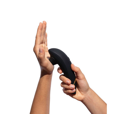 Hand holding a black Womanizer Premium 2 clitoral stimulator against an open palm on white background.