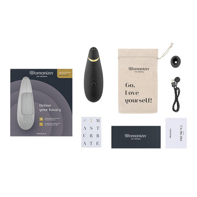 Womanizer Premium 2 clitoral stimulator with box, USB charging cable, two stimulation heads, storage pouch, and user guides laid out on white background.