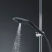 Black Womanizer Wave shower head with water flowing, mounted on chrome shower rail against dark background.