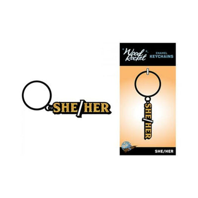 Black and gold enamel keychain with "She/Her" text, displayed loose and on branded Wood Rocket packaging.