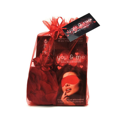 Red organza gift bag containing You & Me silky red blindfold and fabric rose petals for romantic settings.