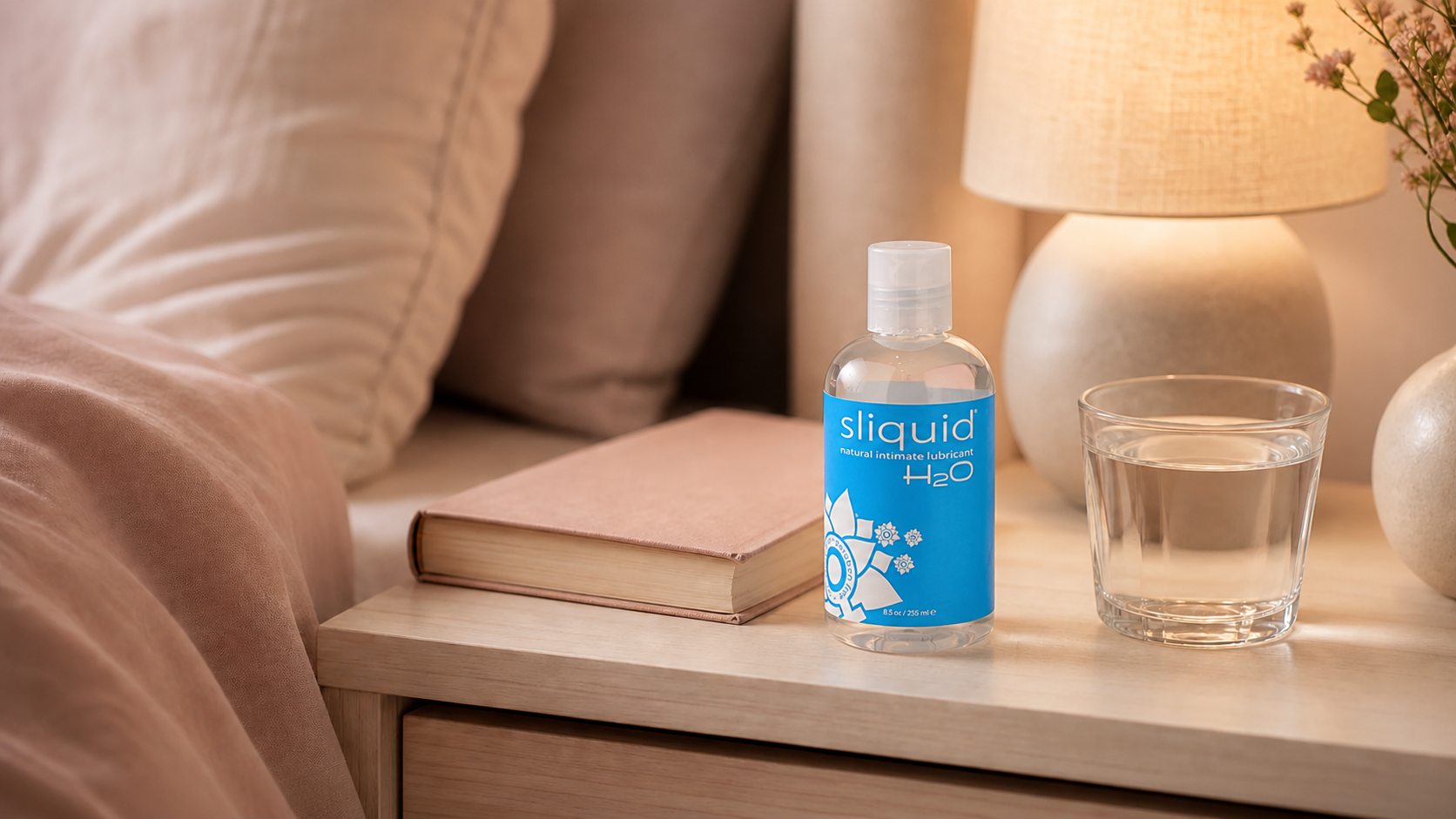 Sliquid H2O lubricant on a bedside table with a book and glass of water